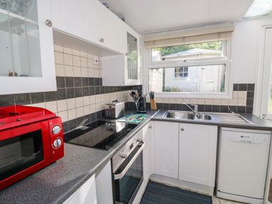 A kitchen with a red microwave oven a stovetop a toaster a kettle a knife block a double sink and a dishwasher at Driftwood Polzeath near Wadebridge