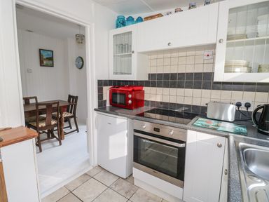 A kitchen with a red microwave on the counter a oven a toaster and a kettle next to a sink with view into adjoining dining room with table and chairs at Driftwood Polzeath near Wadebridge
