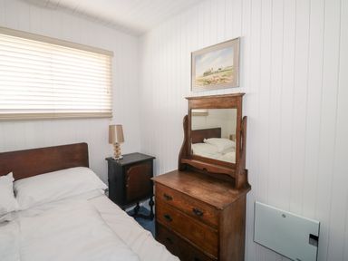 A bedroom with a bed bedside table and a wooden chest of drawers with a mirror at Driftwood Polzeath near Wadebridge