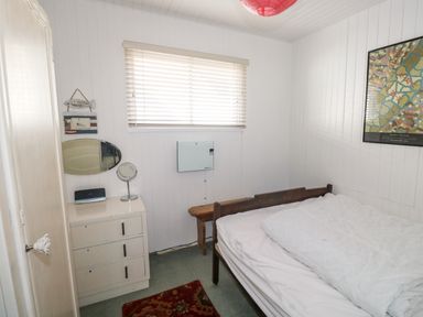 A small bedroom with a bed a chest of drawers with two mirrors a window with blinds and a framed map on the wall at Driftwood in Polzeath near Wadebridge