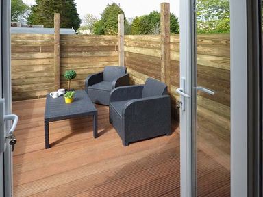 Outdoor wooden deck with two black chairs and a black table with cups and plants at White Cottage Annexe in Tenby