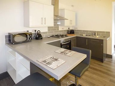 A kitchen with a microwave kettle and toaster on the counter and bar stools at White Cottage Annexe Tenby