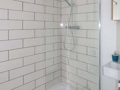 A shower area with white rectangular tiles and a handheld showerhead next to a small white sink with a soap dispenser at White Cottage Annexe in Tenby