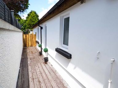 A narrow outdoor walkway with wood decking and white walls on both sides at White Cottage Annexe in Tenby