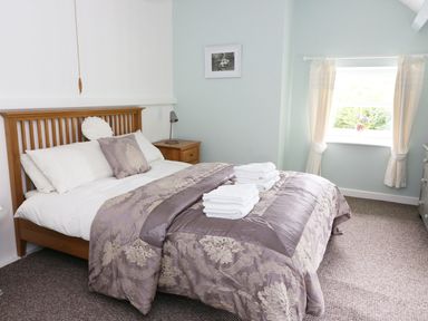 A bedroom with a wooden bed with folded towels on the bed near a window with curtains at Penglanowen Fawr in Llangwyryfon near Aberystwyth