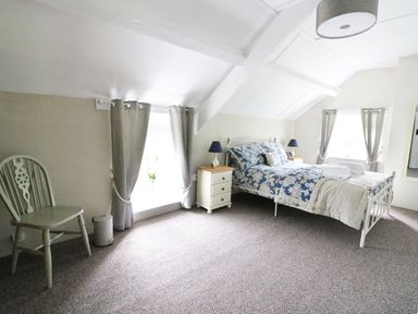 A bedroom with a bed and nightstands with lamps beside windows with curtains at Penglanowen Fawr in Llangwyryfon near Aberystwyth