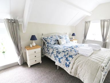 A bedroom with a bed covered in patterned blue and white bedding and two bedside tables with lamps at Penglanowen Fawr in Llangwyryfon near Aberystwyth