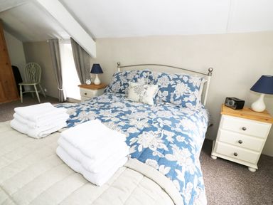 A bedroom with a bed with floral bedding two bedside tables with lamps a chair and folded towels on the bed at Penglanowen Fawr in Llangwyryfon near Aberystwyth
