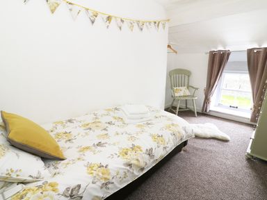 A bedroom with a single bed with floral bedding a wooden chair with a cushion curtains on a window and a carpeted floor at Penglanowen Fawr in Llangwyryfon near Aberystwyth