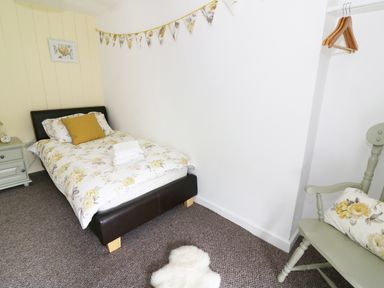 A bedroom with a single bed with floral bedding a bedside table a chair with a floral cushion and wall bunting at Penglanowen Fawr in Llangwyryfon near Aberystwyth