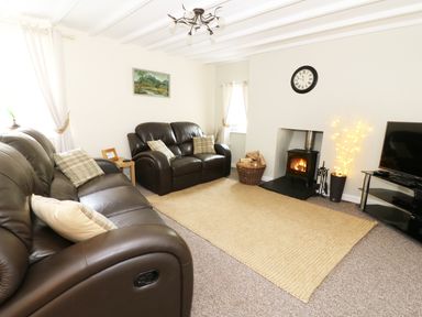 A living room with brown leather sofas a wall clock a fireplace and a television at Penglanowen Fawr in Llangwyryfon near Aberystwyth