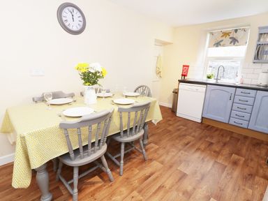 A kitchen with a dining table set with plates and glasses and blue cabinets at Penglanowen Fawr in Llangwyryfon near Aberystwyth