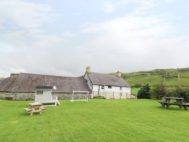 A grassy yard with picnic tables and a small playhouse near a white stone building at Penglanowen Fawr in Llangwyryfon near Aberystwyth