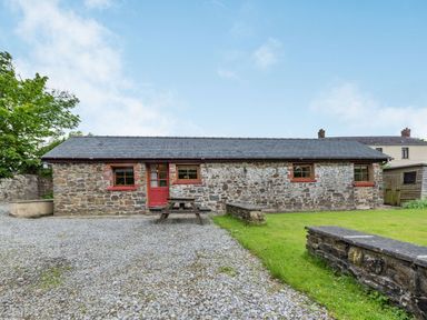 A stone cottage with a slate roof a red door and three windows with a picnic bench on a gravel area and grass at Cilwen Fach in Cynwyl Elfed