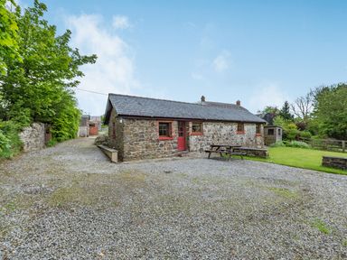 A stone cottage with a slate roof and red door surrounded by gravel driveway and green trees at Cilwen Fach in Cynwyl Elfed