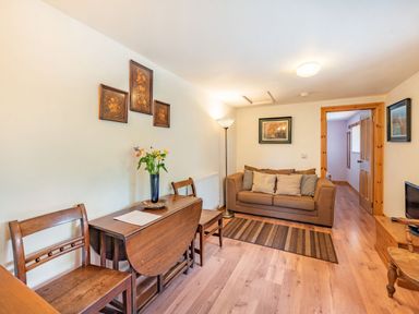 A living room with a brown sofa cushions a wooden dining table with chairs and a floor lamp at Cilwen Fach in Cynwyl Elfed