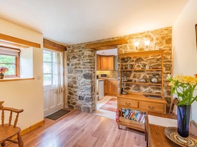 A room with wooden furniture stone walls an entrance door and a view into a kitchen at Cilwen Fach in Cynwyl Elfed