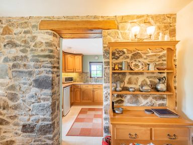 A stone wall with wooden doorway leading to a kitchen and a wooden shelf unit with metal teapots and plates at Cilwen Fach in Cynwyl Elfed