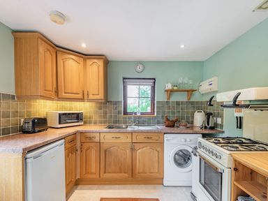 A kitchen with wooden cabinets a washing machine a stove and a small window at Cilwen Fach in Cynwyl Elfed