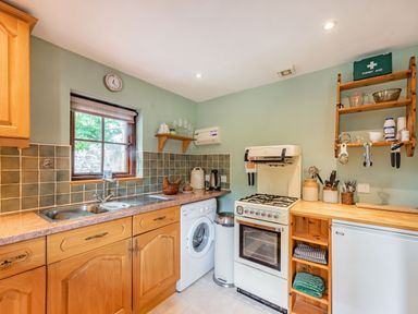 A kitchen with wooden cabinets a washing machine a stove a small fridge and shelves with kitchen utensils at Cilwen Fach in Cynwyl Elfed