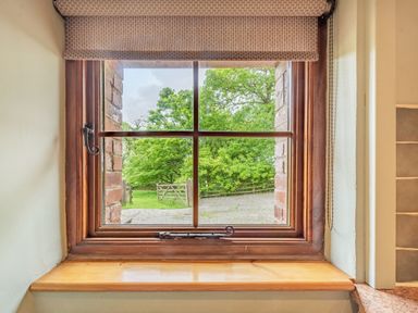 A wooden framed window with a roller blind overlooking a garden with trees and a gate at Cilwen Fach in Cynwyl Elfed