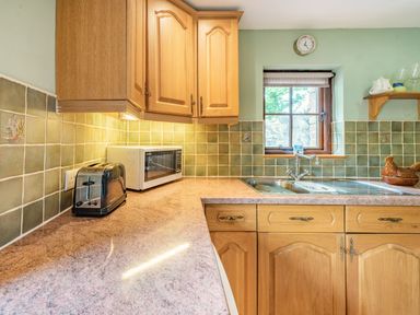 A kitchen with wooden cabinets a toaster microwave sink and tiled backsplash at Cilwen Fach in Cynwyl Elfed
