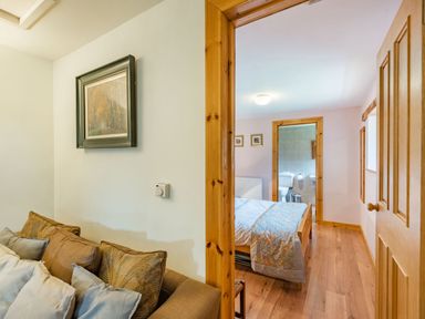 A view from a living room with sofa and cushions into a bedroom with a bed and an en suite bathroom showing a toilet at Cilwen Fach in Cynwyl Elfed