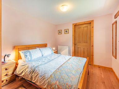A bedroom with a double bed bedside tables lamps wooden door and hardwood floor at Cilwen Fach in Cynwyl Elfed