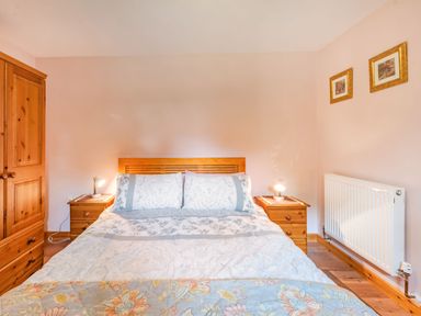 A bedroom with a double bed flanked by two wooden nightstands with lamps and a wooden wardrobe in Cilwen Fach Cynwyl Elfed