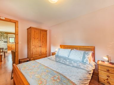 A bedroom with a wooden bed and floral bedspread two wooden nightstands with lamps and a wooden wardrobe at Cilwen Fach in Cynwyl Elfed