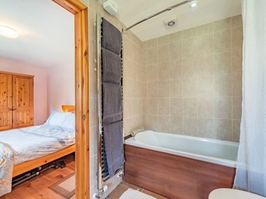 A bathroom with a bathtub and towels hanging on a radiator next to a bedroom with a bed and wooden wardrobe at Cilwen Fach in Cynwyl Elfed