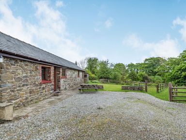 A stone building with red window frames next to a gravel area with a picnic table and a fenced garden at Cilwen Fach in Cynwyl Elfed