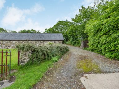 A gravel driveway next to a stone wall with greenery and a stone building in the background at Cilwen Fach in Cynwyl Elfed