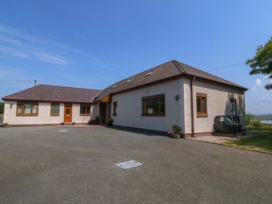 An exterior view of a one-story house with brown roof tiles and several windows with wooden frames at Fferam Y Llyn in Rhosgoch near Cemaes Bay