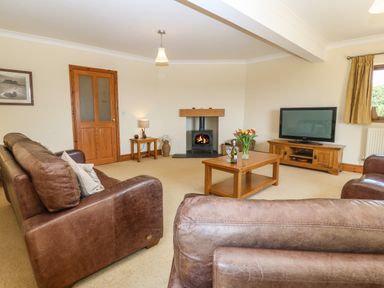 A living room with brown leather sofas a wooden coffee table a television on a wooden stand a fireplace and a wooden door at Fferam Y Llyn in Rhosgoch near Cemaes Bay