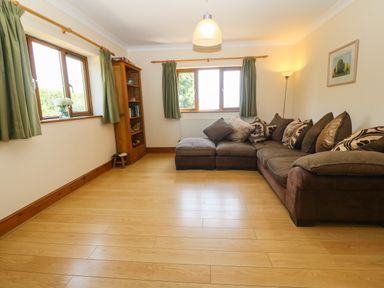 A living room with a sectional sofa and a wooden bookshelf at Fferam Y Llyn in Rhosgoch near Cemaes Bay