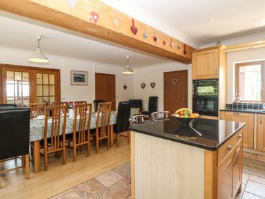 A kitchen and dining area with a wooden dining table and chairs a kitchen island with fruit bowl and wooden cabinets at Fferam Y Llyn in Rhosgoch near Cemaes Bay