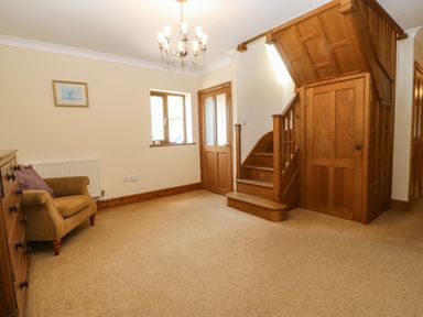 A room with a wooden staircase and under stairs storage a wooden door a window an armchair and a wooden chest of drawers at Fferam Y Llyn in Rhosgoch near Cemaes Bay