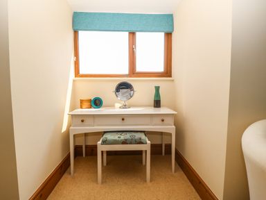 A small desk with a stool under a window with a blue blind a round mirror a blue clock a wooden box and a vase on the desk at Fferam Y Llyn in Rhosgoch near Cemaes Bay