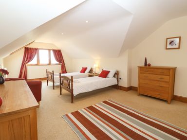 A bedroom with two single beds a wooden dresser a wooden chest of drawers and striped rug at Fferam Y Llyn in Rhosgoch near Cemaes Bay