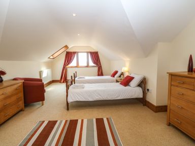 A bedroom with two single beds red cushions and wooden dressers at Fferam Y Llyn in Rhosgoch near Cemaes Bay