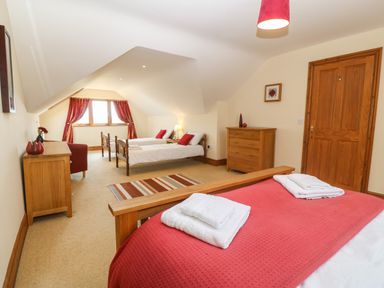 A bedroom with wooden beds, dressers, red curtains, and folded towels at Fferam Y Llyn in Rhosgoch near Cemaes Bay