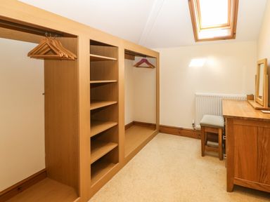 A dressing room with wooden shelves hangers a stool a desk and a skylight window at Fferam Y Llyn in Rhosgoch near Cemaes Bay