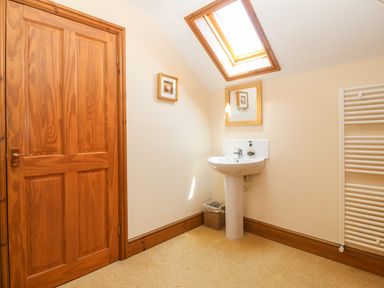 A bathroom with a wooden door a white pedestal sink a wall mirror skylight and a white towel radiator at Fferam Y Llyn in Rhosgoch near Cemaes Bay