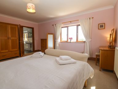 A bedroom with a bed with folded towels a wooden wardrobe a chest of drawers a mirror and a window with white curtains at Fferam Y Llyn in Rhosgoch near Cemaes Bay