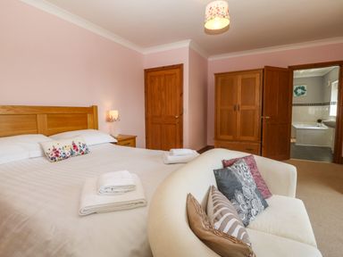 A bedroom with a double bed a white sofa with cushions wooden wardrobe a door leading to a bathroom at Fferam Y Llyn in Rhosgoch near Cemaes Bay