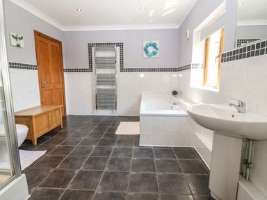 A bathroom with a bathtub sink wooden door and cabinet at Fferam Y Llyn in Rhosgoch near Cemaes Bay