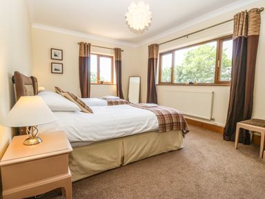 A bedroom with two twin beds bedside table and lamp windows with curtains at Fferam Y Llyn in Rhosgoch near Cemaes Bay