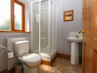 A bathroom with a toilet, shower enclosure, pedestal sink, and a window at Fferam Y Llyn in Rhosgoch near Cemaes Bay