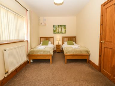 A bedroom with two single beds a window radiator and a wooden door at Fferam Y Llyn in Rhosgoch near Cemaes Bay